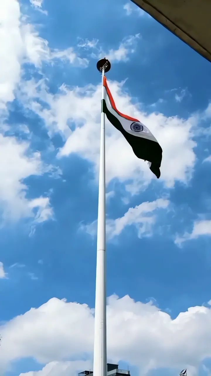 Indian Flag Flying High Against Blue Sky With White Clouds